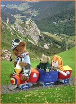 Photo of Milligan Bear driving a toy train with a rag doll across a mountain range