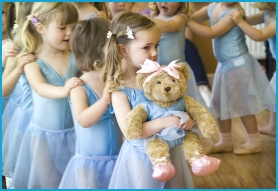 Young children in a long line with their hands on each others shoulders learning to dance