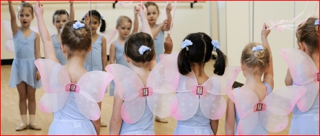 Photo of ballet children in wings and holding wands looking at themselves in a mirror